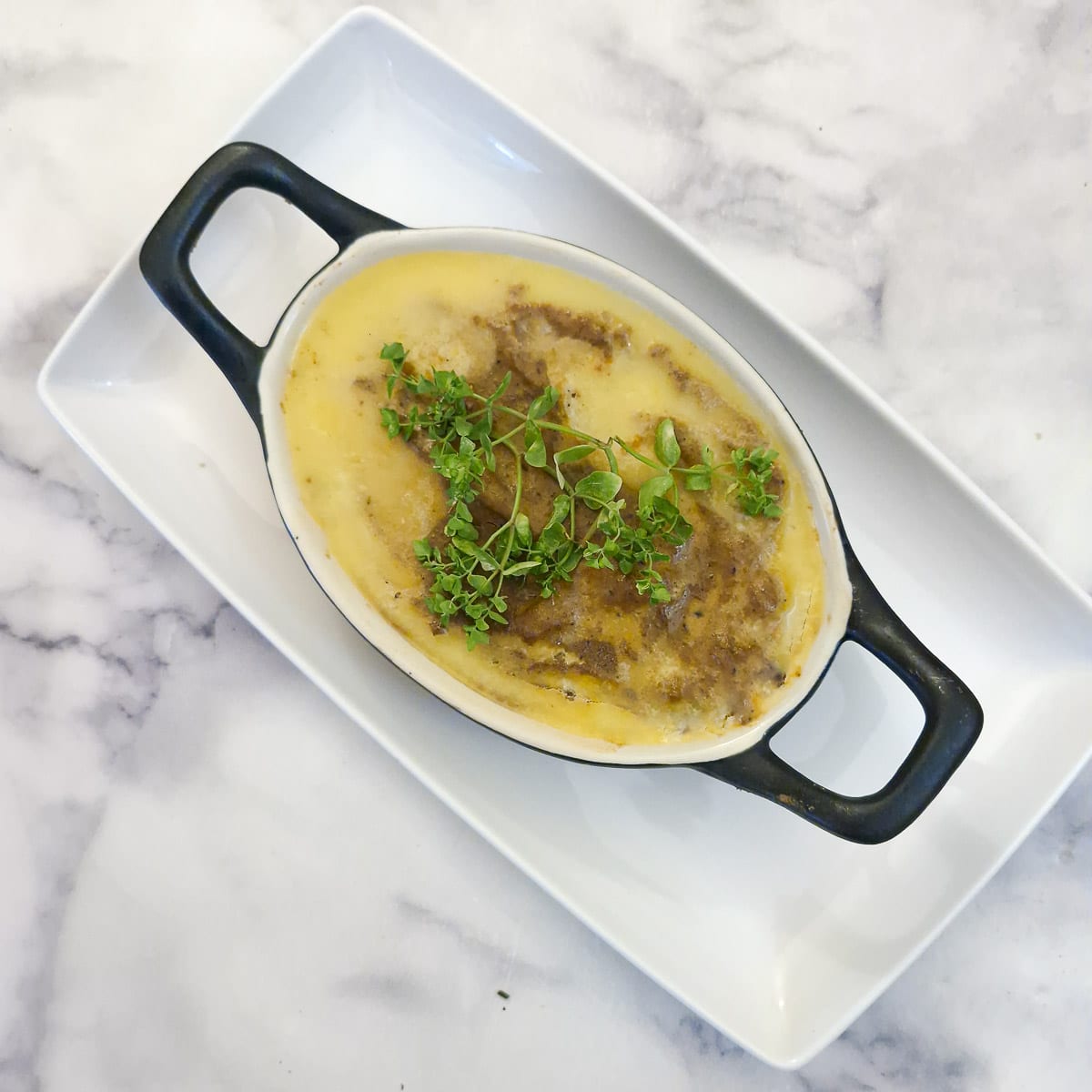 Overhead shot of a black oval dish oduck lever pate on a white platter. The pate has been sealed with butter and garnished with fresh thyme.