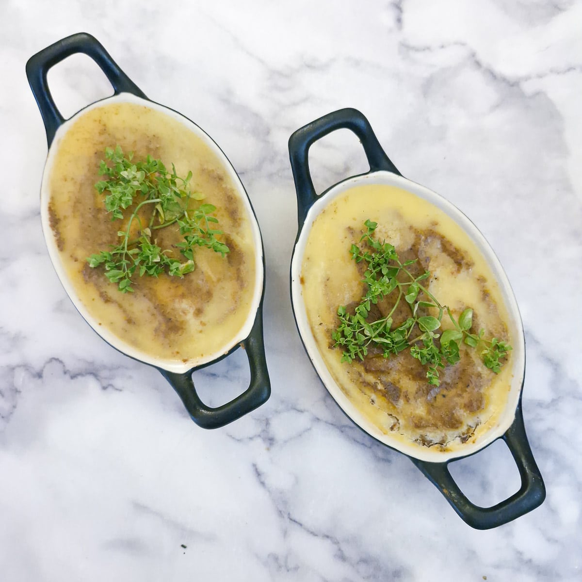 2 small back oval dishes filled with duck liver pate that has been covered in melted butter and garnished with sprigs of fresh thyme.