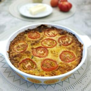 A crustless mortadella ,cheese and tomato quiche in a round baking dish.