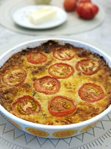 A crustless mortadella ,cheese and tomato quiche in a round baking dish.