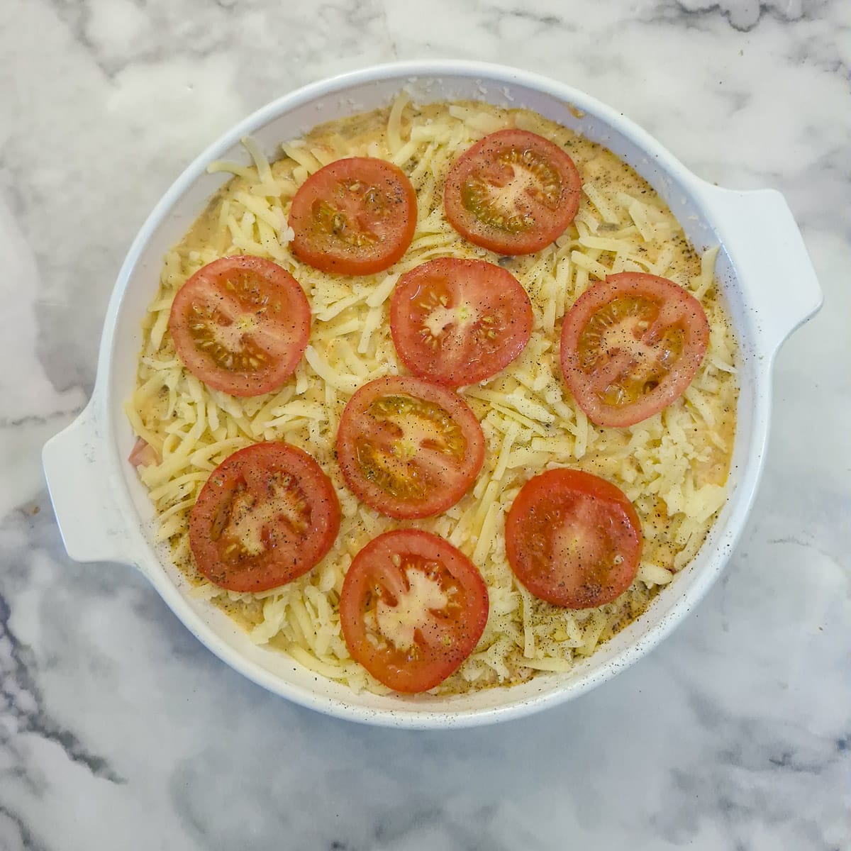Grated cheese and sliced tomatoes arranged on top of the unbaked quiche.