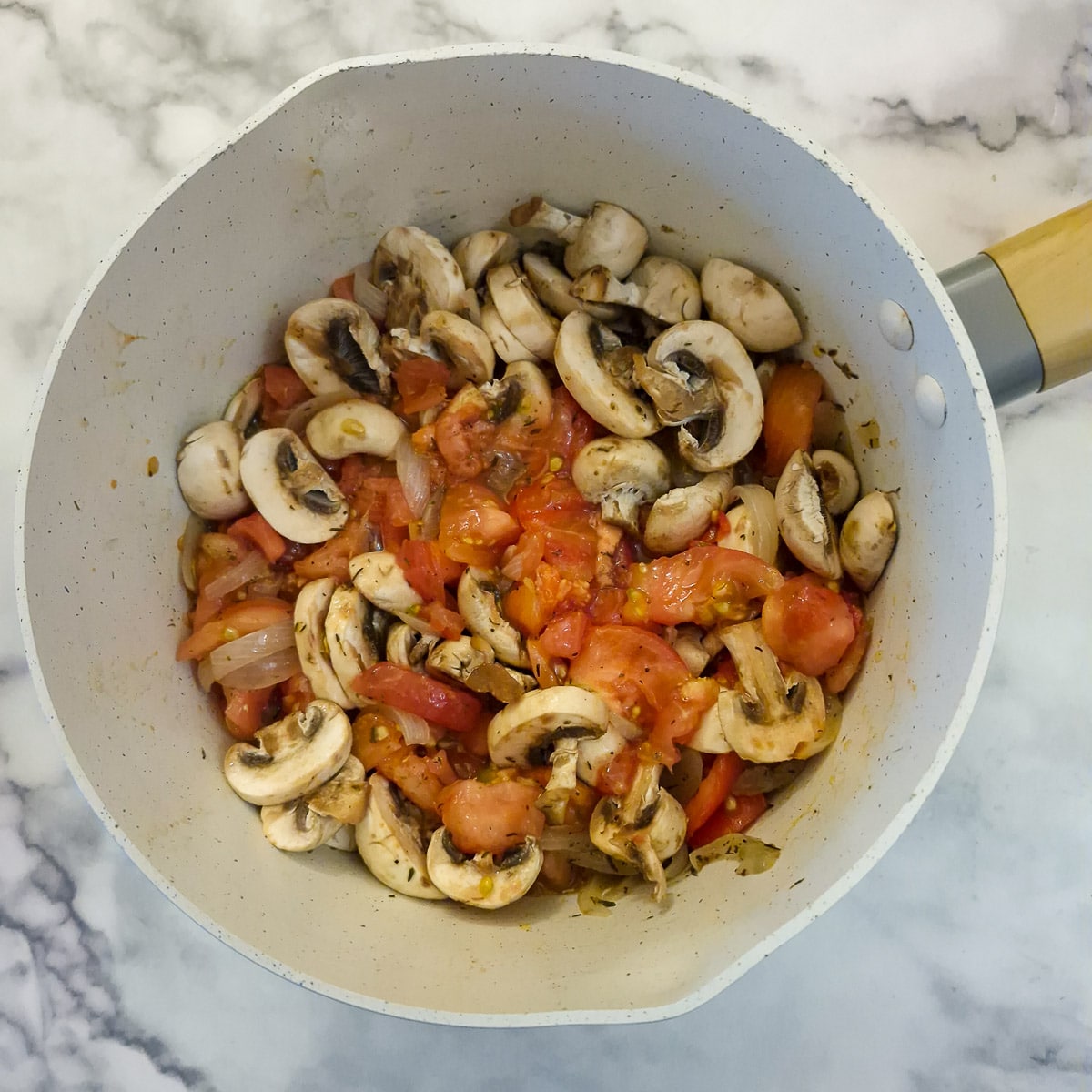 Mushrooms and tomatoes added to the saucepand of onions.
