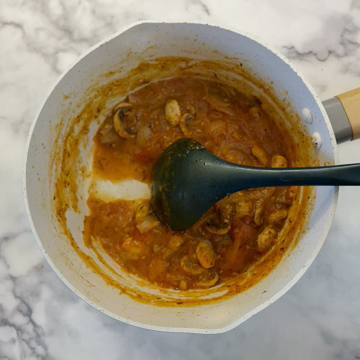 A large spoon being drawn through the tomato mixture showing how it leaves a trail.