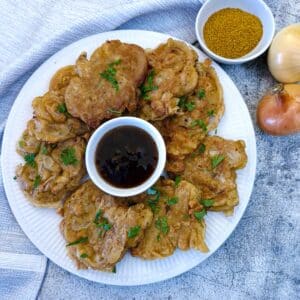 A large white plate with crispy onion fritters arranged around a small dish of dipping sauce.