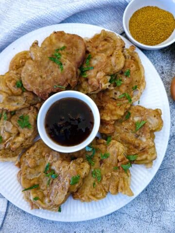 A large white plate with crispy onion fritters arranged around a small dish of dipping sauce.