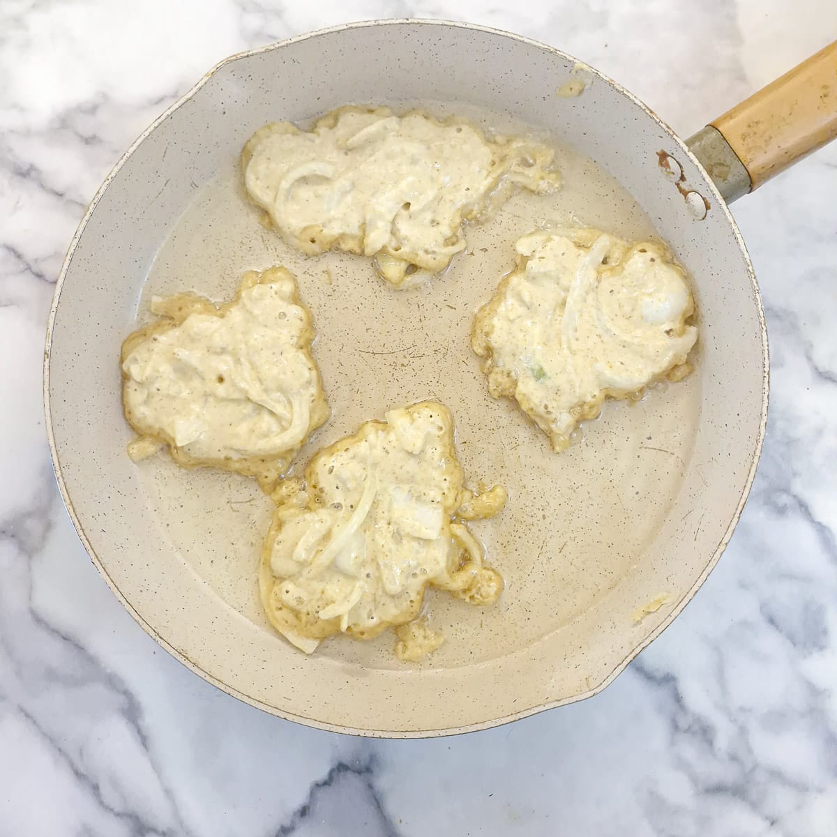 Step 6, 4 onions fritters starting to brown in a frying pan.