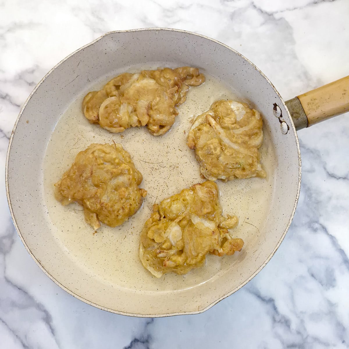 Step 7, 4 browned crispy onion fritters in a frying pan.