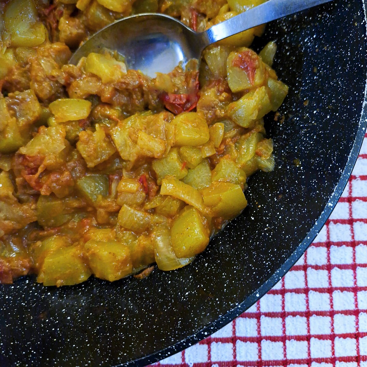 Close up of marrow and tomato curry in a wok, with a serving spoon.