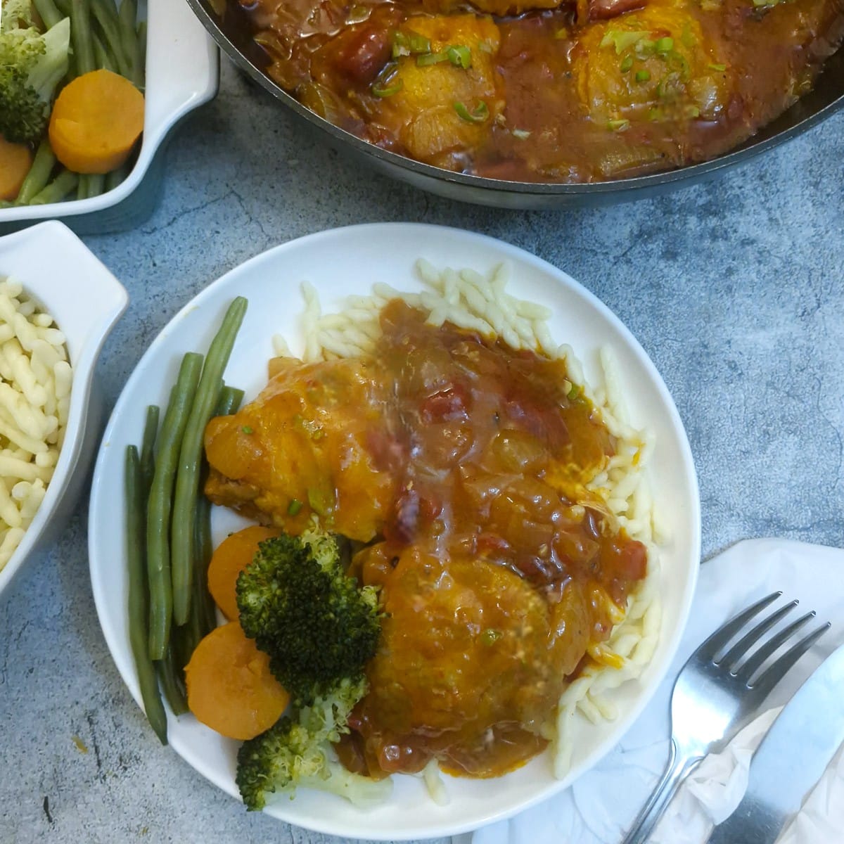 Chicken paprikash on a white plate with noodles, vegetables and lots of gravy.