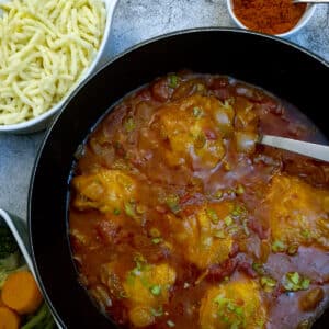 Chicken paprikash in a black dish showing pieces of chicken submerged in a rich gravy.