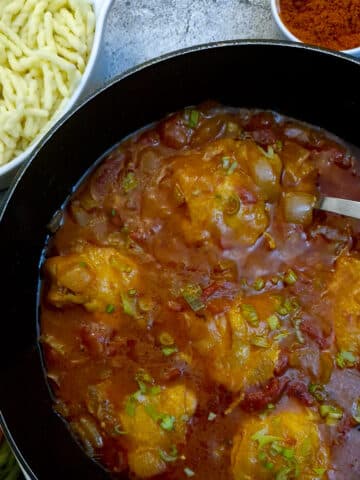 Chicken paprikash in a black dish showing pieces of chicken submerged in a rich gravy.