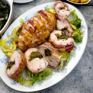 Sliced hunterr's chicken a la canard on a serving platter next to an unsliced bacon-wrapped chicken breast.