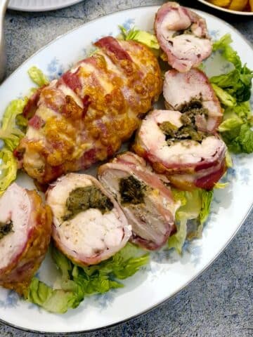 Sliced hunterr's chicken a la canard on a serving platter next to an unsliced bacon-wrapped chicken breast.