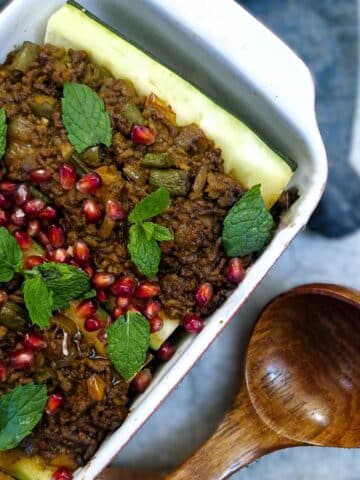 A dish of lamb keema stuffed marrows garnished with pomegranate seeds and mint leaves.