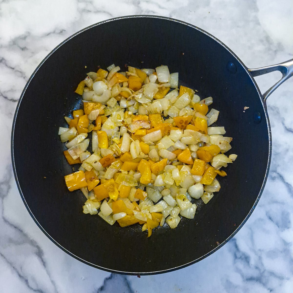 Onions and peppers softening in a large pan.