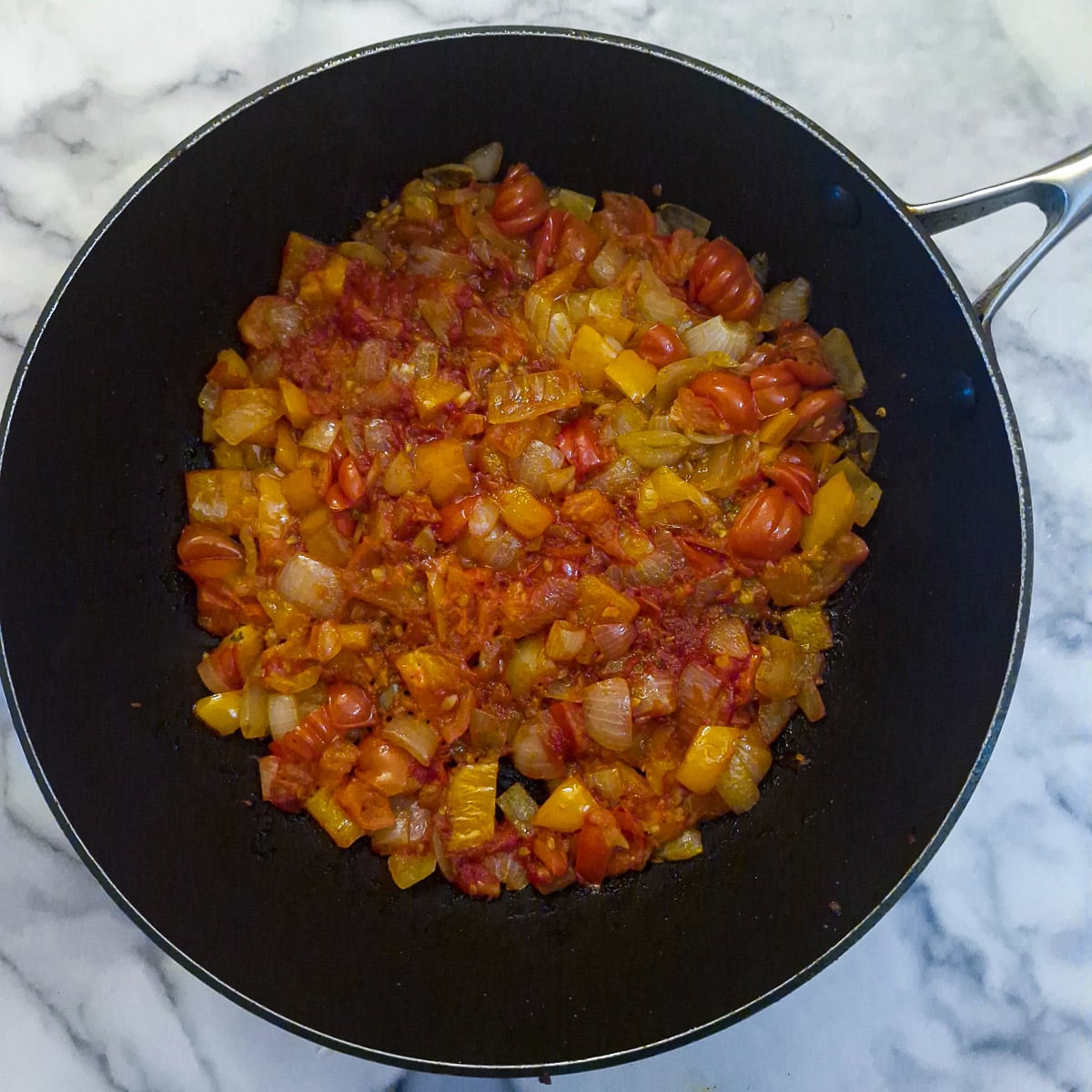 Tomatoes softening in the same pan with the onions and peppers,