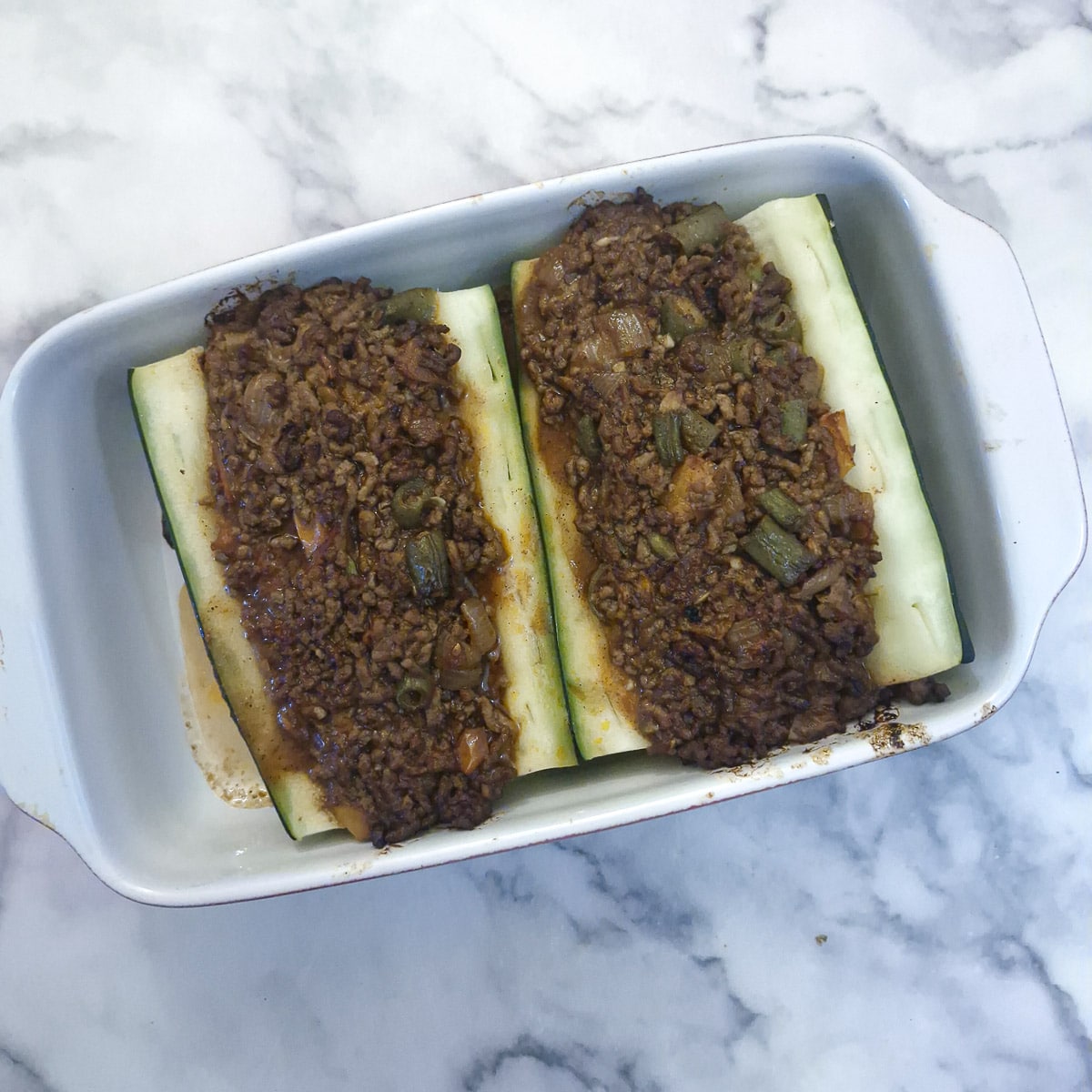 A baking dish with 2 large pieces of cooked marrow stuffed with lamb keema.