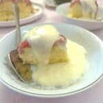 A slice of microwave strawberry sponge pudding on a white plate with custard.