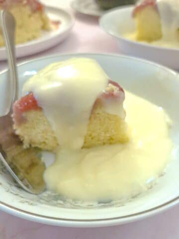 A slice of microwave strawberry sponge pudding on a white plate with custard.
