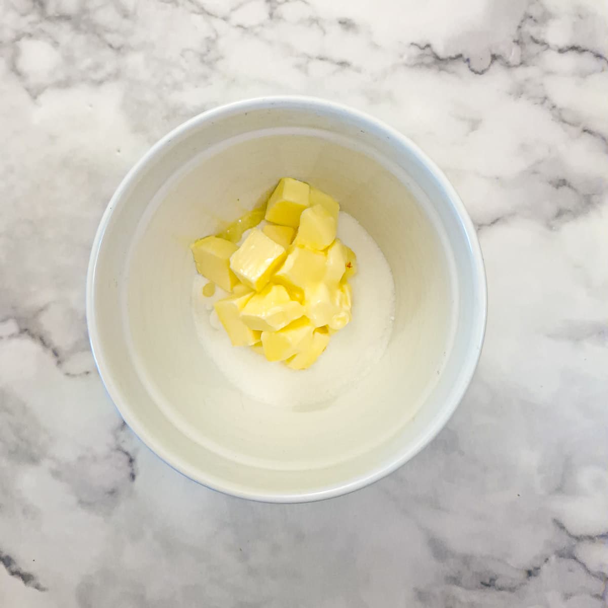 Cubed butter and sugar in a mixing bowl.