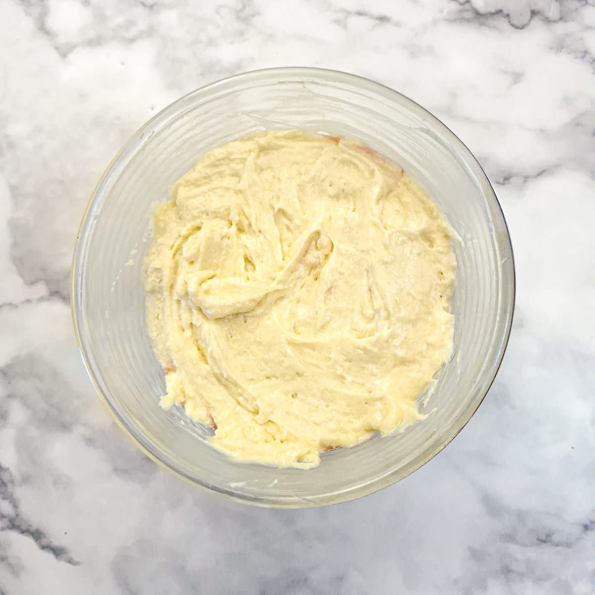 Sponge pudding batter spooned over strawberries in a glass bowl.