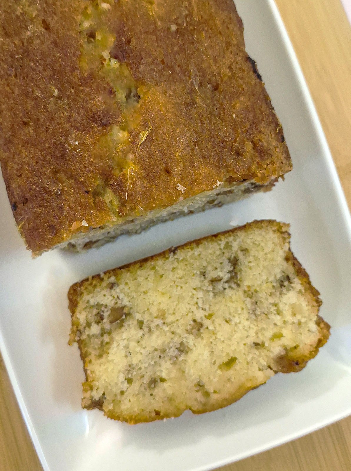 Overhead shot of an orange drizzle cake, on a white platter, with a slice of cake cut from the loaf.