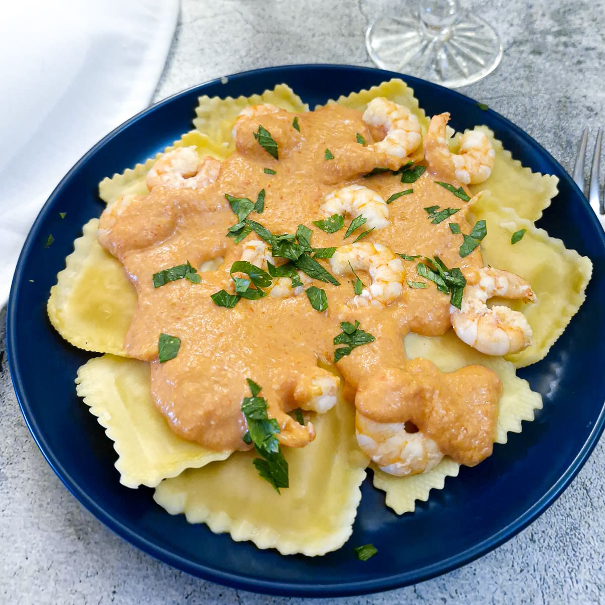 Close up of a plate of ravioli topped with red pepper sauce and garnished with prawns and parsley.