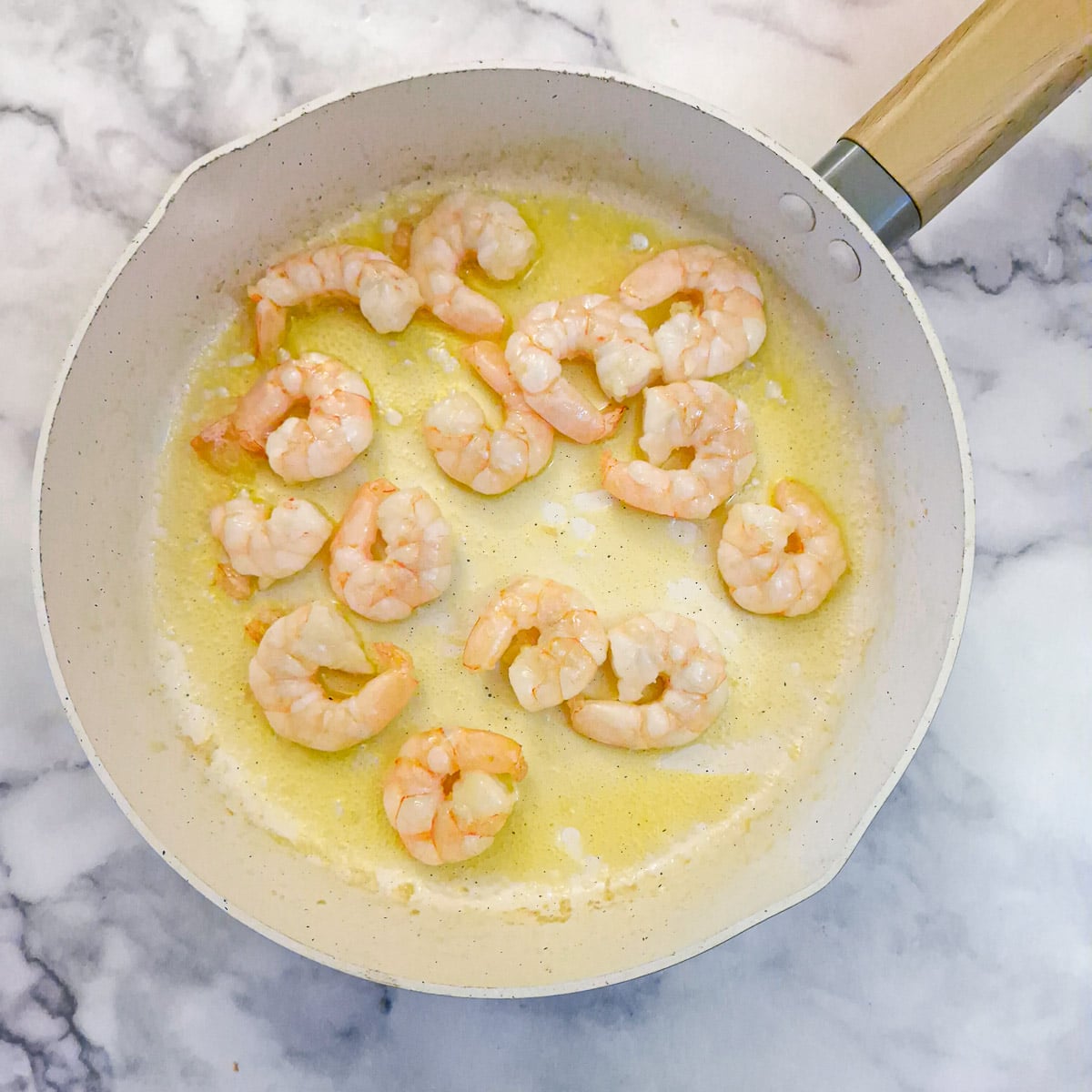 Prawns turning pink in butter in a frying pan.