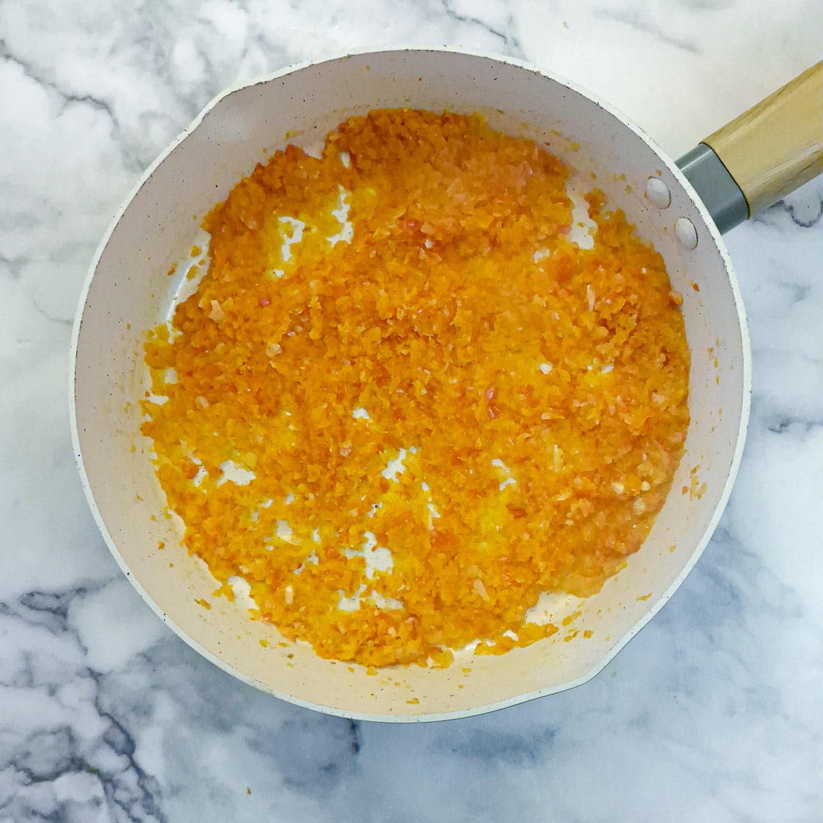 Finely chopped red pepper and onion softening in a frying pan.