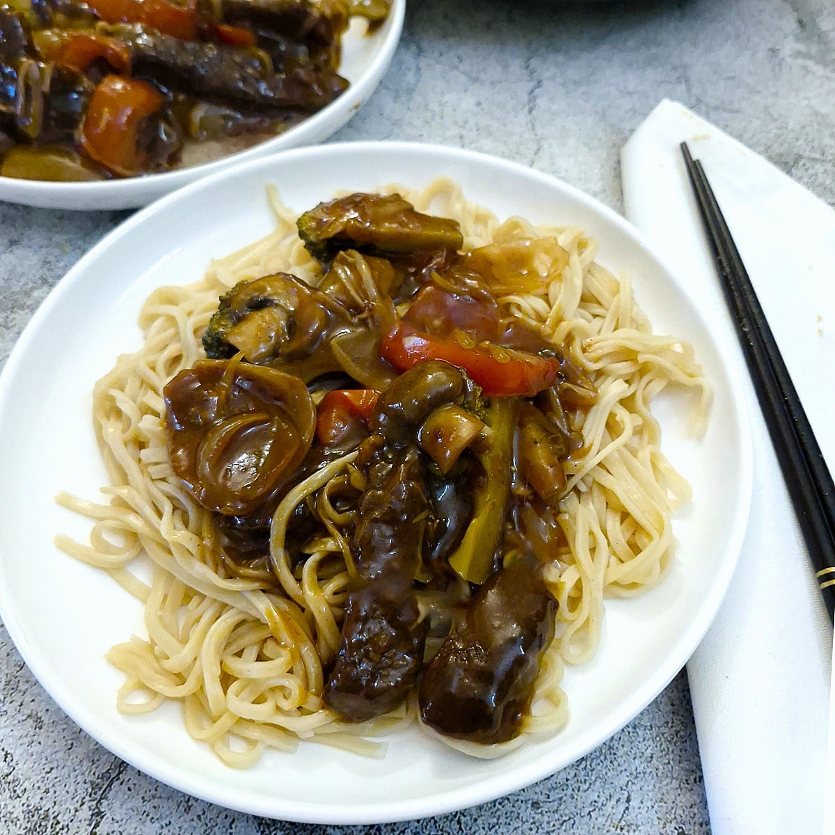 A helping of beef strips in garlic sauce piled on top of a plate of Chinese noodles.