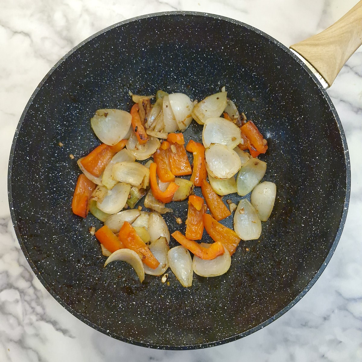Onions and red peppers softening in a wok.