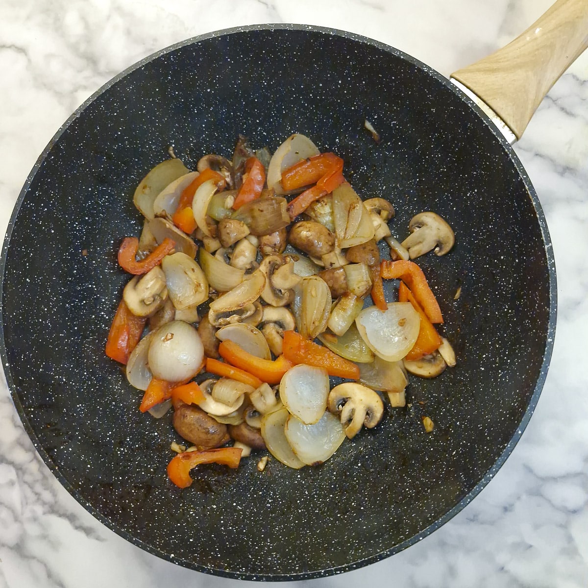 Mushrooms cooking with onions and red pepper in a wok.