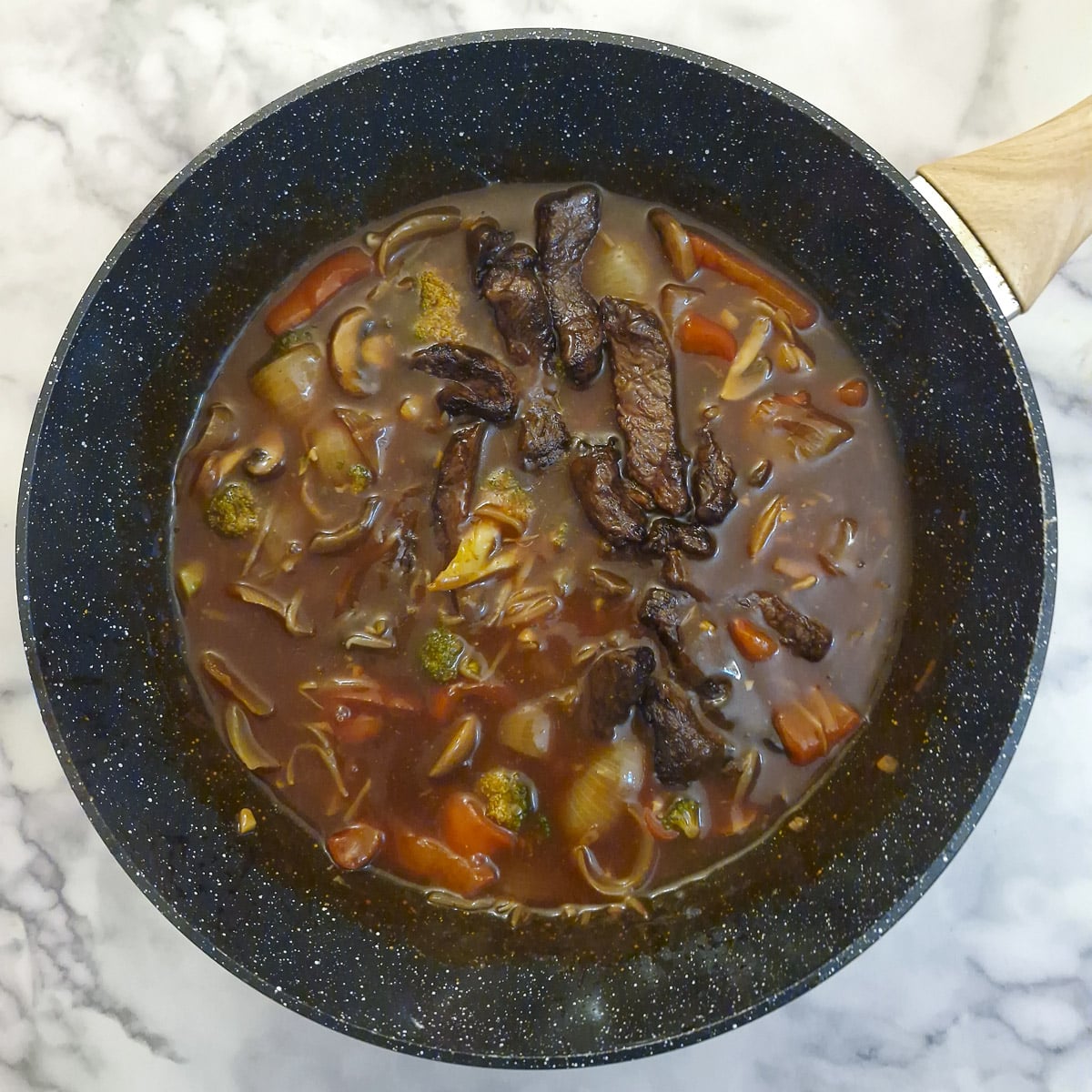 Steak strips added to the sauce in a wok.