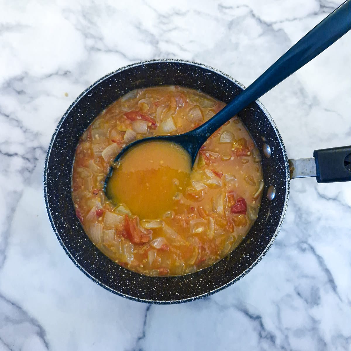 Tomato stew which has been si9mmering for 30 minutes in a large pan. There is a spoon in the pan showing the liquid content.