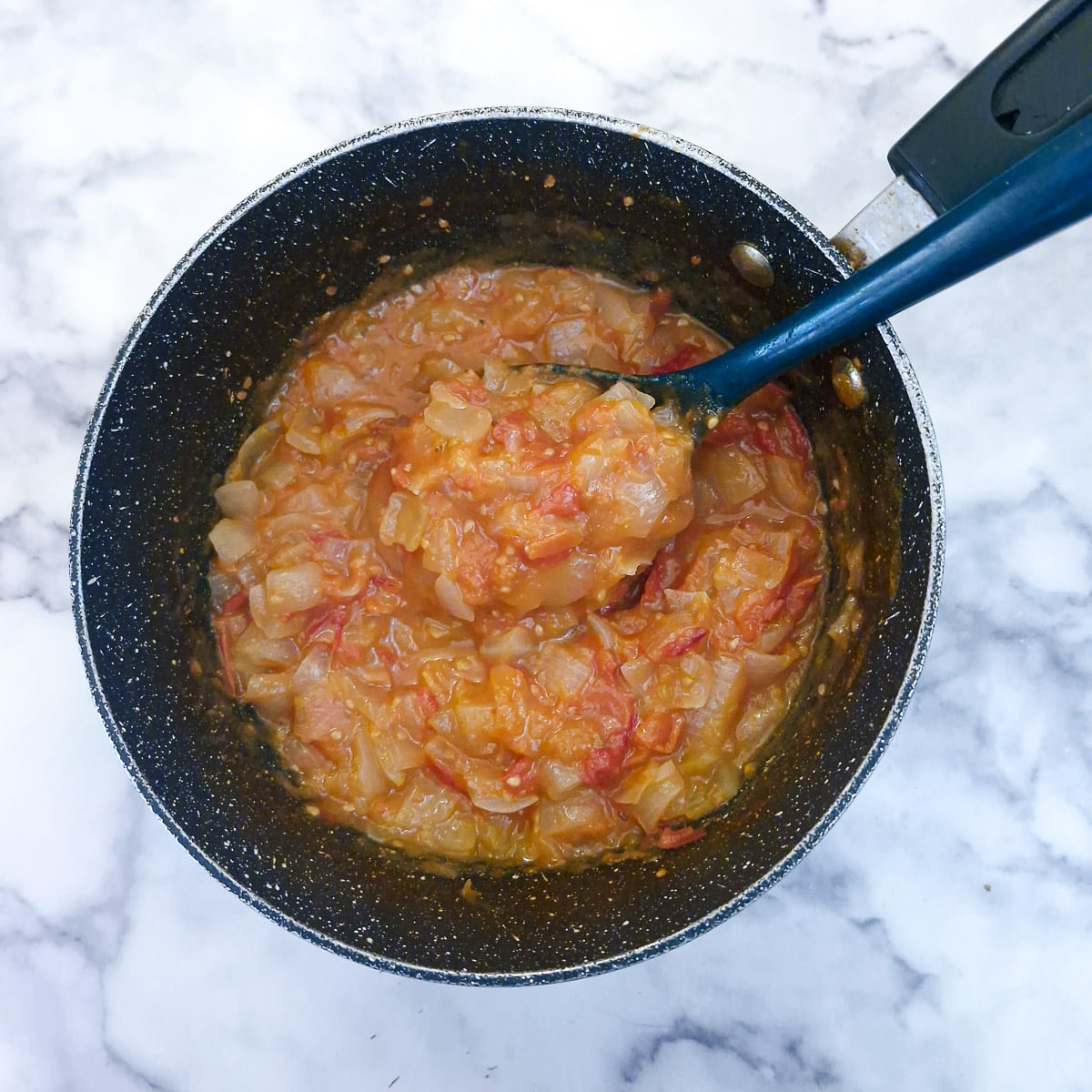Fully cooked tomato and onion stew in a large pan showing the consistency.