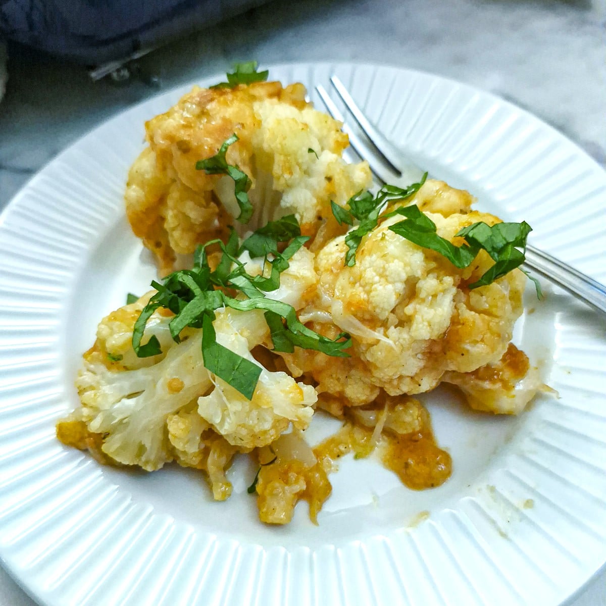 A helping of cheesy cauliflowere bake garnished with chopped parsley on a white plate.