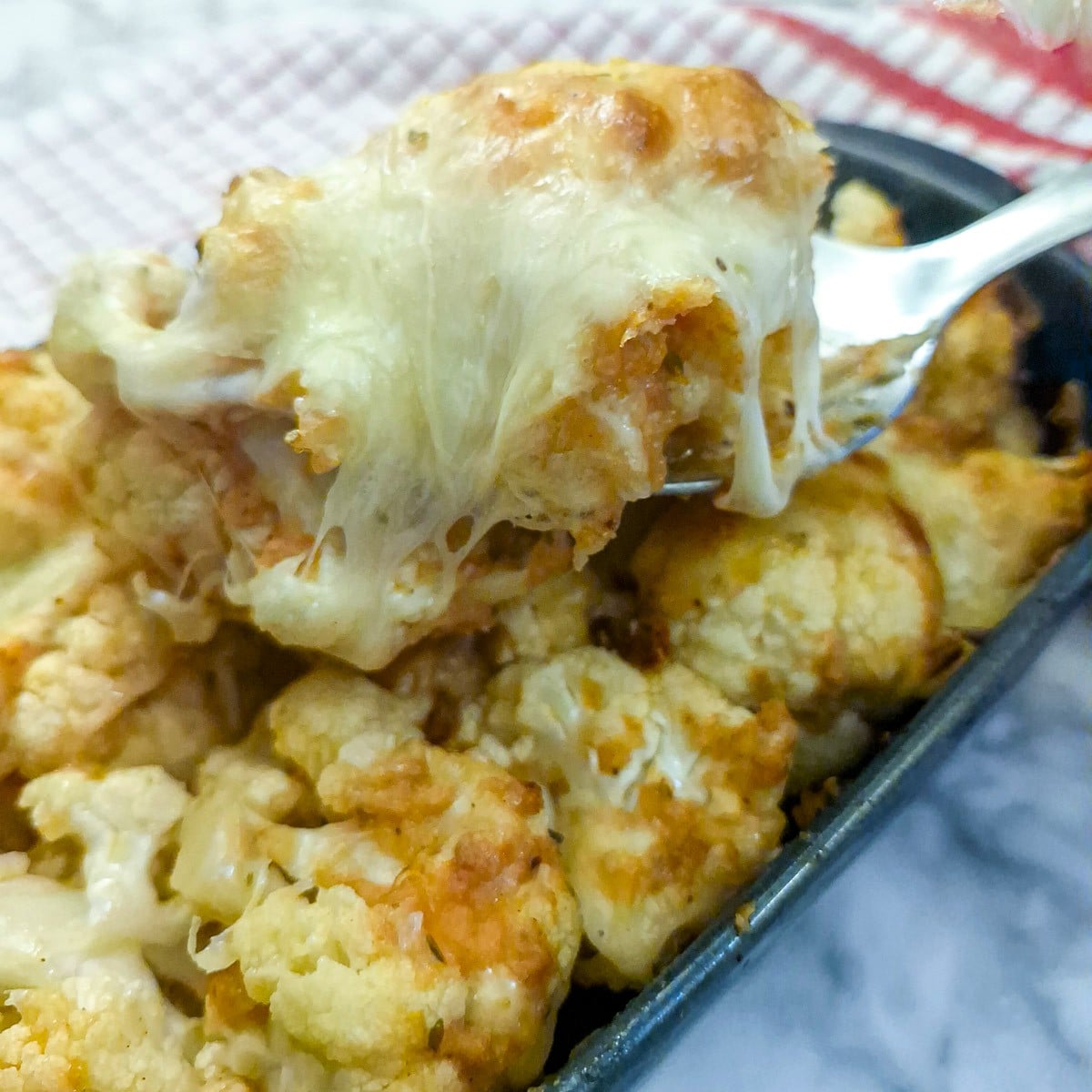 A spoonful of cauliflower being lifted from the dish. You can clearly see the stretchy melted mozzarella cheese.