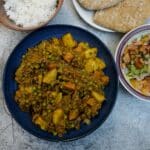 A bowl of curried minced beef (curry in a hurry) on a table with bowls of rice and salad in the background.
