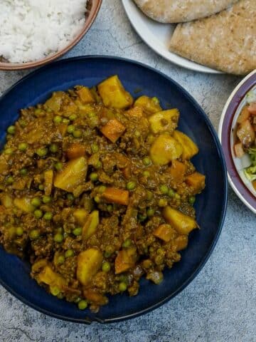 A bowl of curried minced beef (curry in a hurry) on a table with bowls of rice and salad in the background.