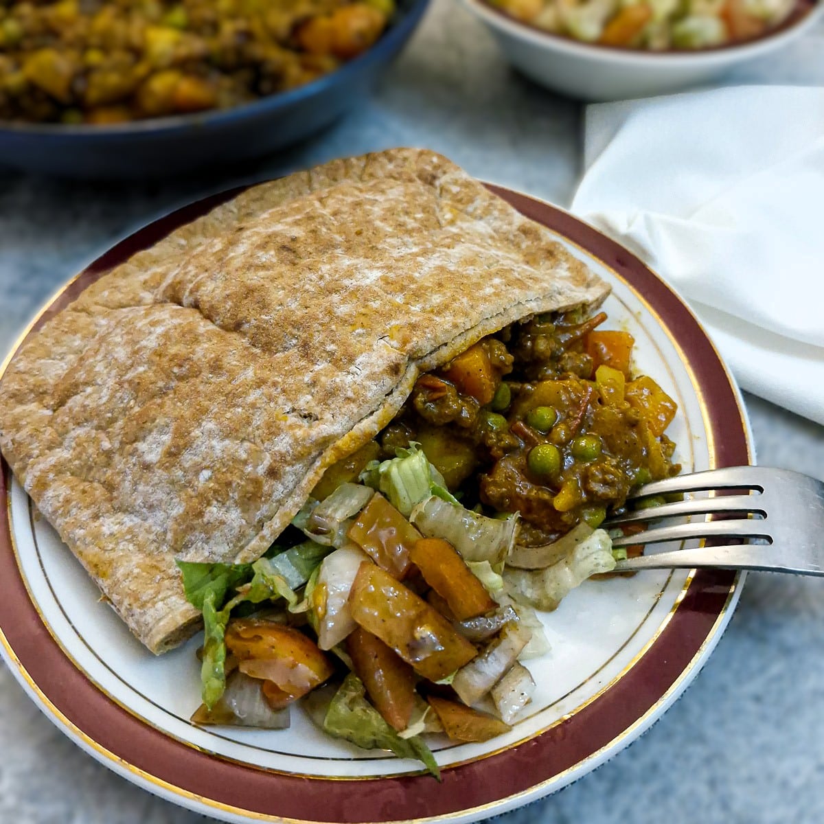 A wholewheat pita bread stuffed with curry and balsamic tomato salad on a red-rimmed plate.