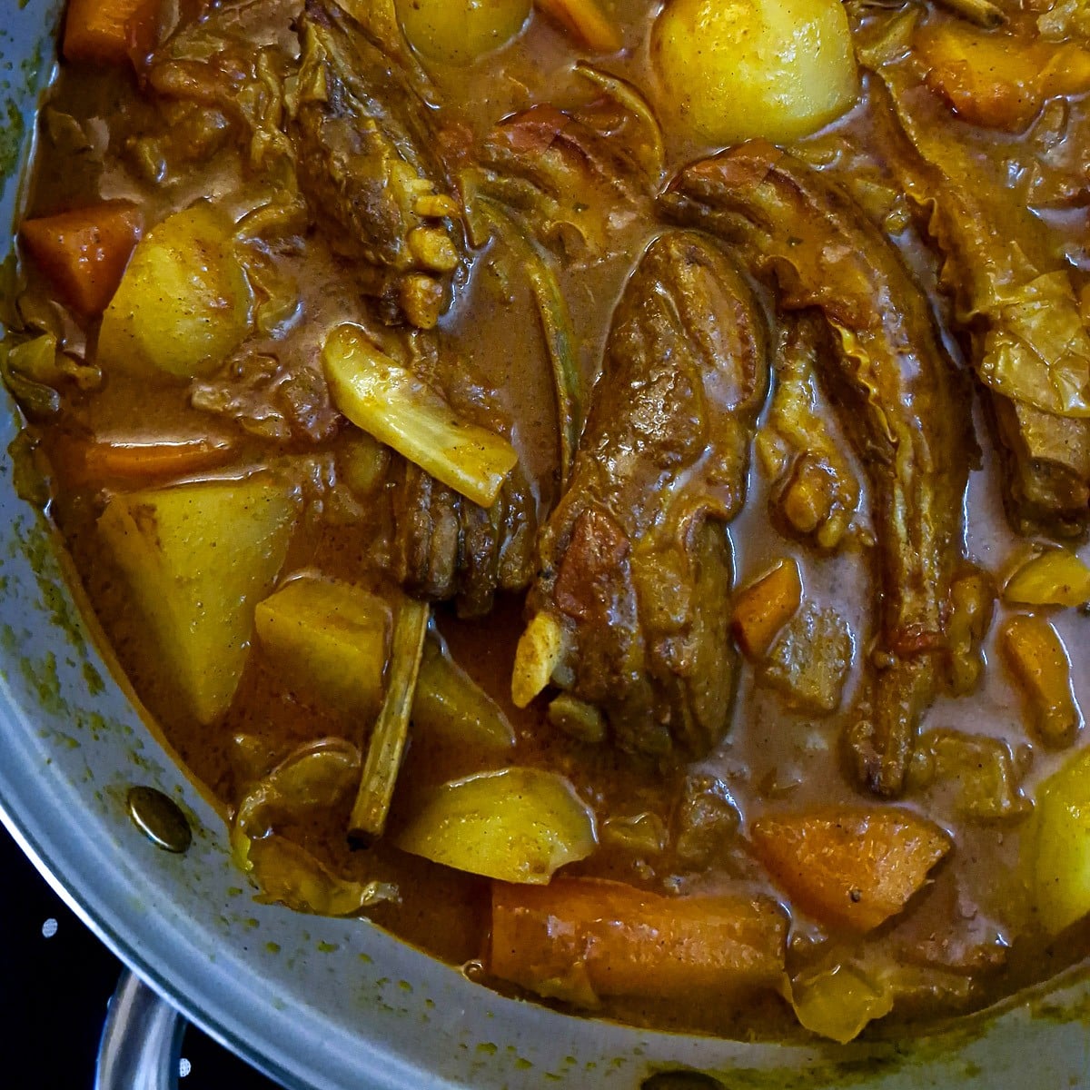 Close up of succulent lamb ribs in curry sauce with potatoes and carrots.