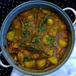 A large pan of lamb rib curry with plenty of potatoes and carrots in a thick curry sauce.