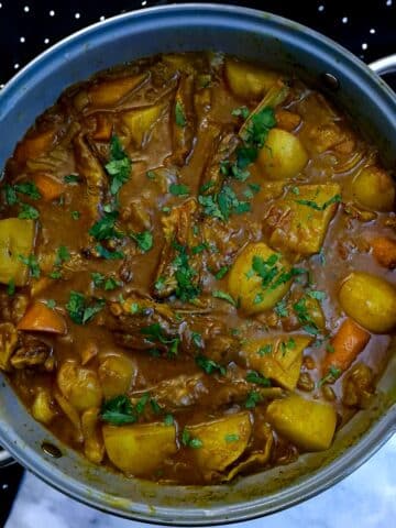A large pan of lamb rib curry with plenty of potatoes and carrots in a thick curry sauce.