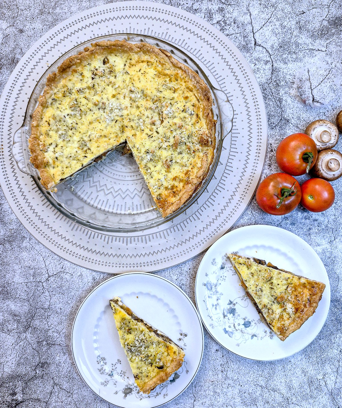 Overhead shot of an egg and tomato quiche with 2 side plates each holding a slice of quiche.