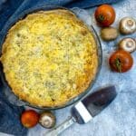 Overhead shot of an egg and tomato quiche on table with fresh tomatoes and onions.