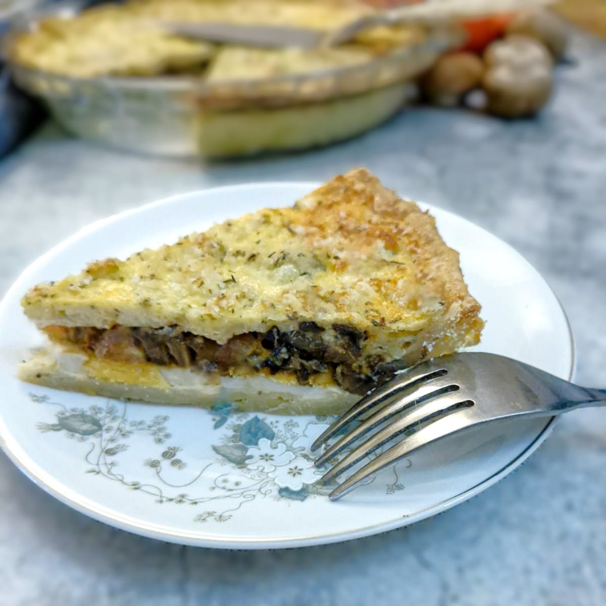 A slice of quiche on a flower patterned plate.
