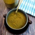 Homemade curry powder in a brown dish on a table with a jar of curry powder in the background.