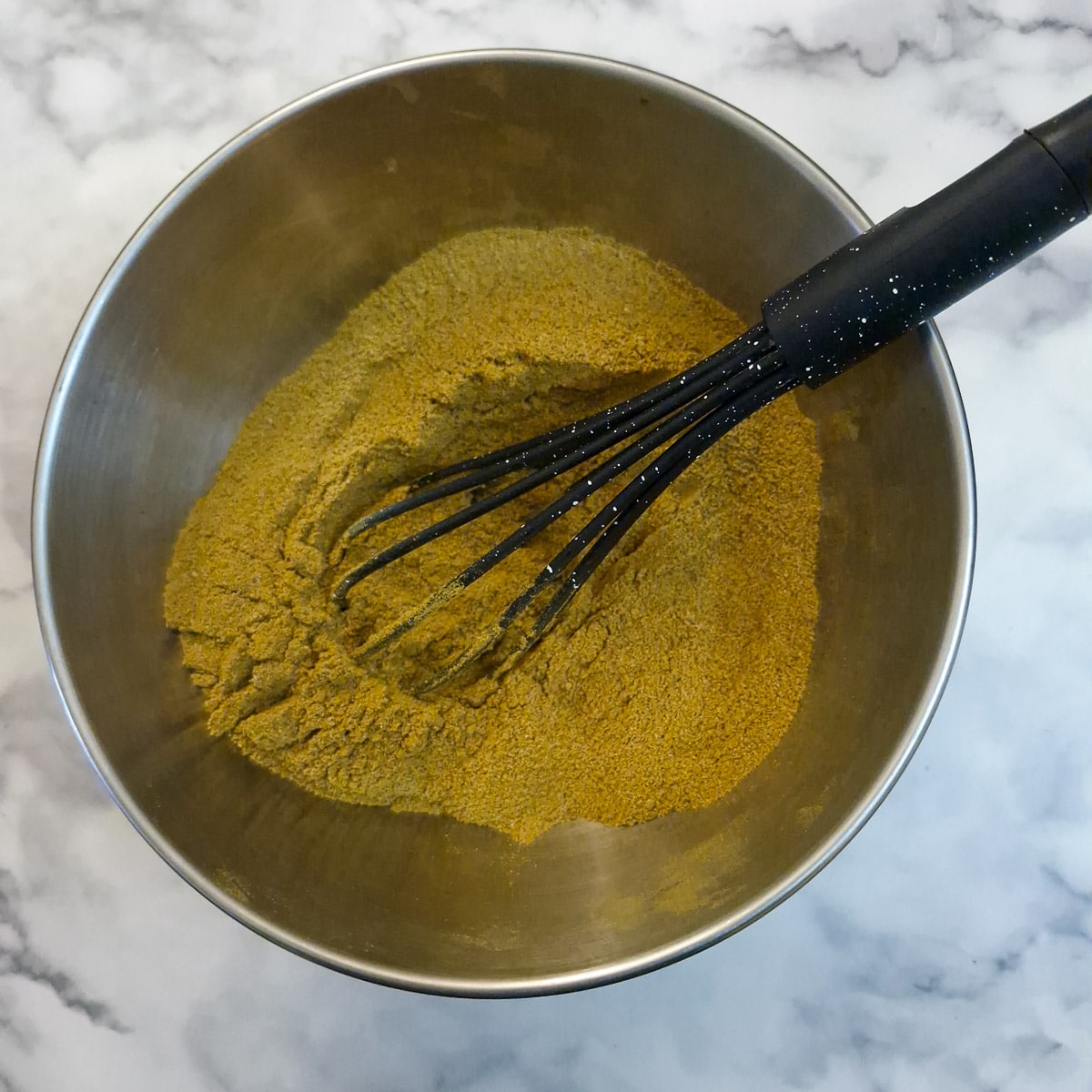 Curry spices being mixed with a balloon whisk in a metal bowl.