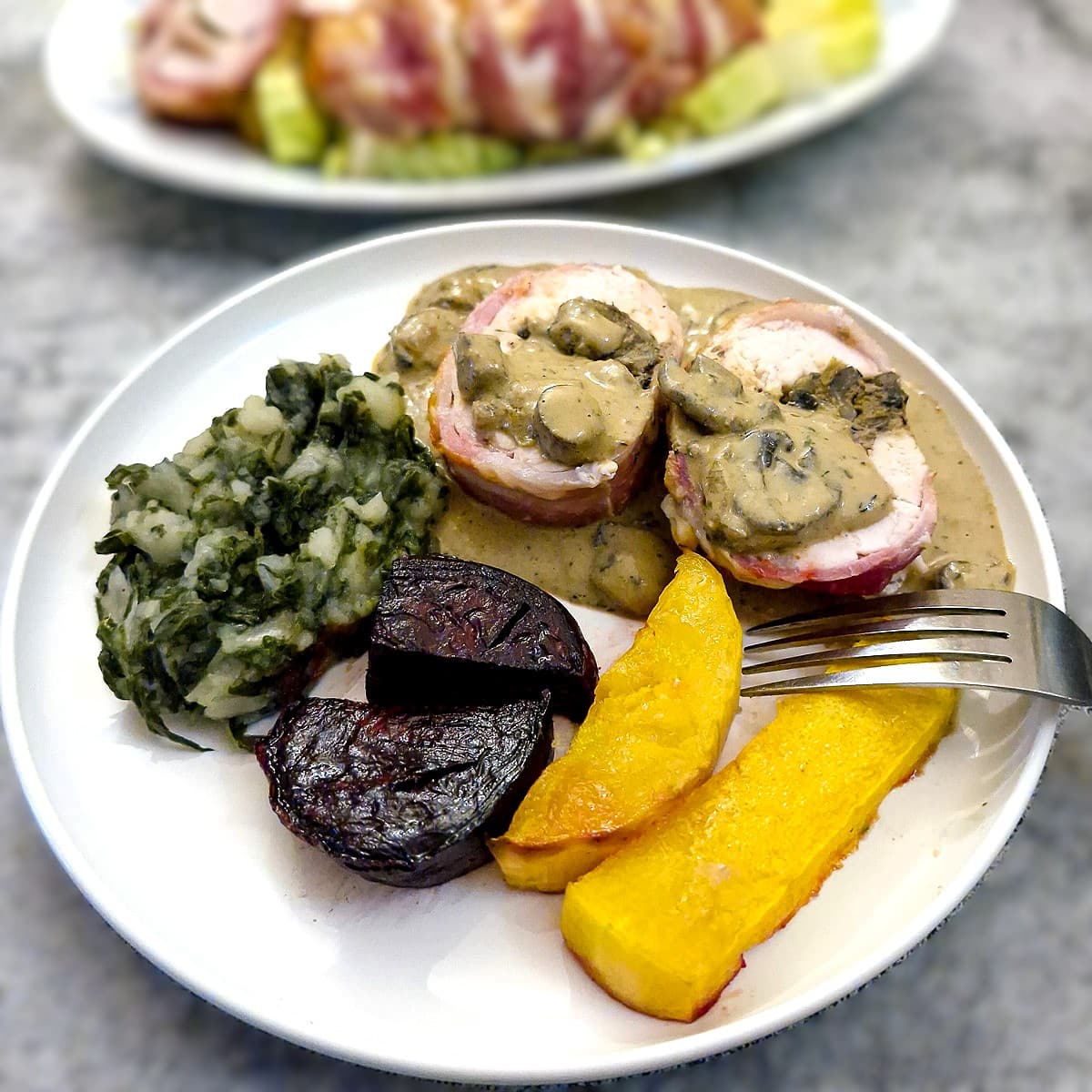 Two medallions of chicken a la canard on a white plate, with spinach mash, roasted beetroot and butternut. The mushroom and pate sauce has been poured over the chicken.