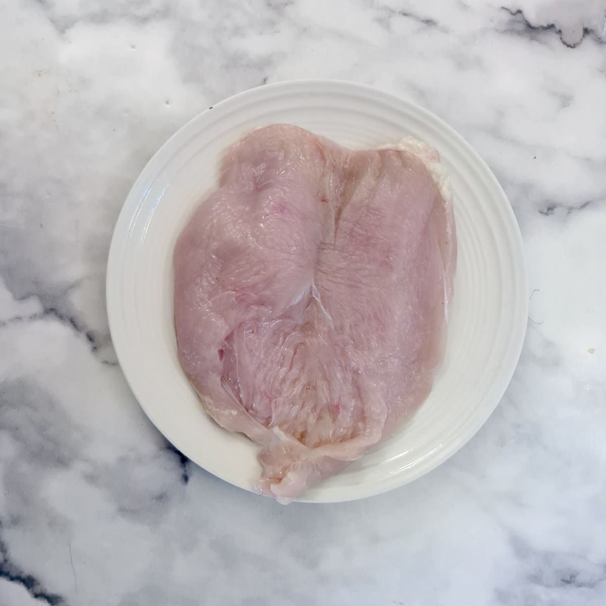 Step 5, a chicken breast butterflied on a white plate.